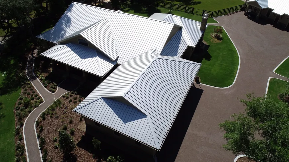 Aerial view of a light-colored metal roof with intersecting roof planes and a chimney